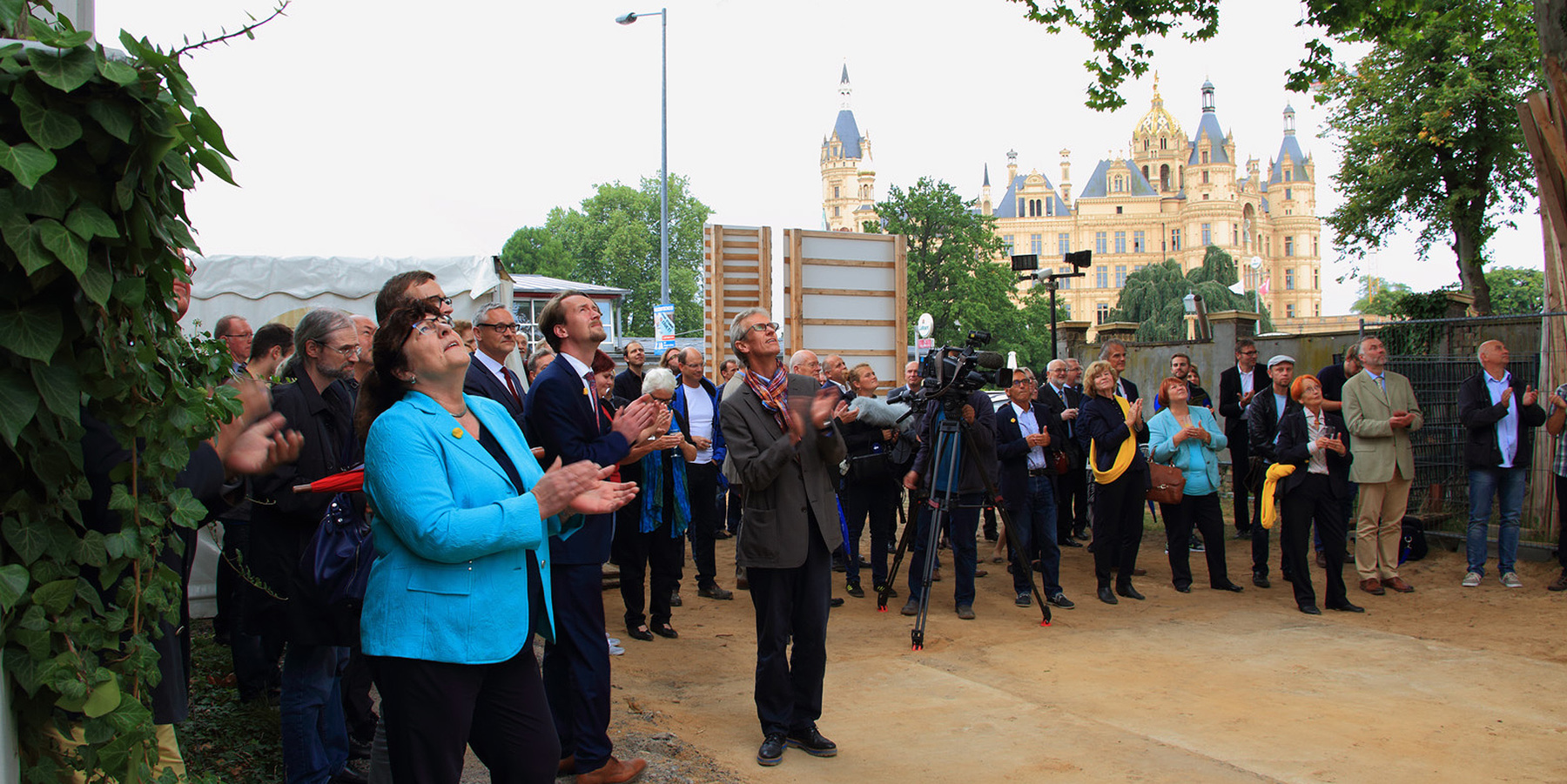 Hinten das Schloss Schwerin, vorn die Finanzministerin Heike Polzin, Abteilungsleiter Stefan Wenzl, Kultusminister Mathias Brodkorb, Museumsleiter Dirk Blübaum sowie die weiteren Gäste des Richtfestes und oben - nicht im Bild - der Richtkranz, der in den  © 2015 Betrieb für Bau und Liegenschaften Mecklenburg-Vorpommern