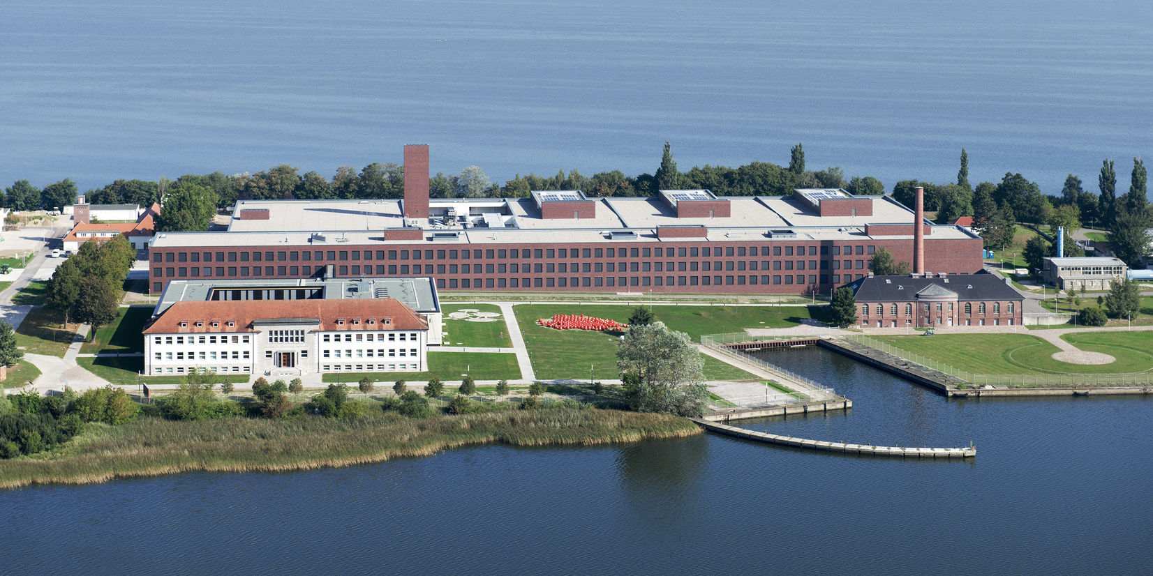 Luftaufnahme der Bundesforschungsanstalt auf der Insel Riems - im Vordergrund links das Hauptgebäude mit dem dahinterliegenden Karree, rechts das alte Heizhaus und im Hintergrund das Laborgebäude mit dem langgestreckten Stallgebäude. © Marion Schmieding/ Alexander Obst