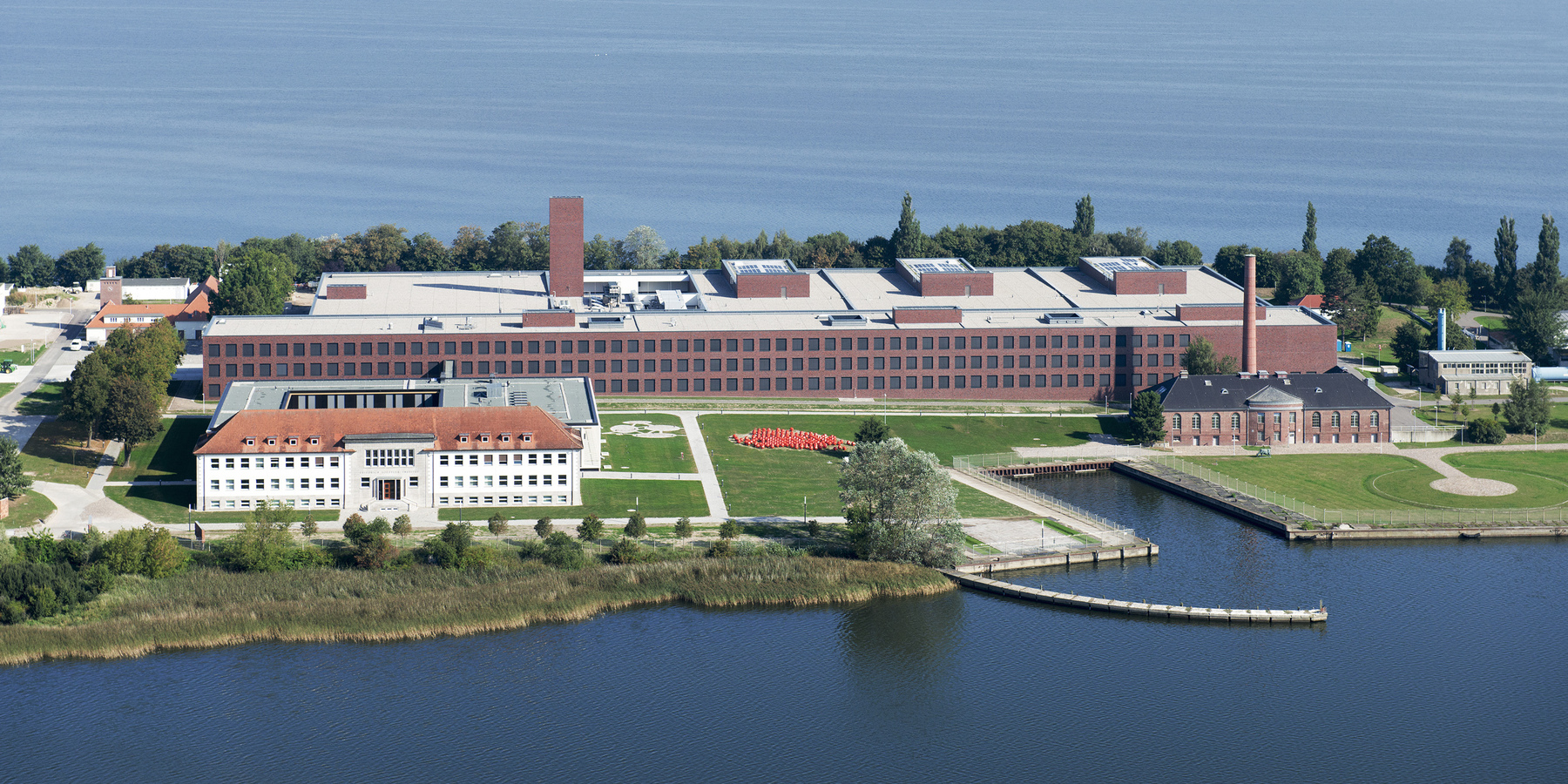 Luftaufnahme der Bundesforschungsanstalt auf der Insel Riems - im Vordergrund links das Hauptgebäude mit dem dahinterliegenden Karree, rechts das alte Heizhaus und im Hintergrund das Laborgebäude mit dem langgestreckten Stallgebäude. © Marion Schmieding/ Alexander Obst