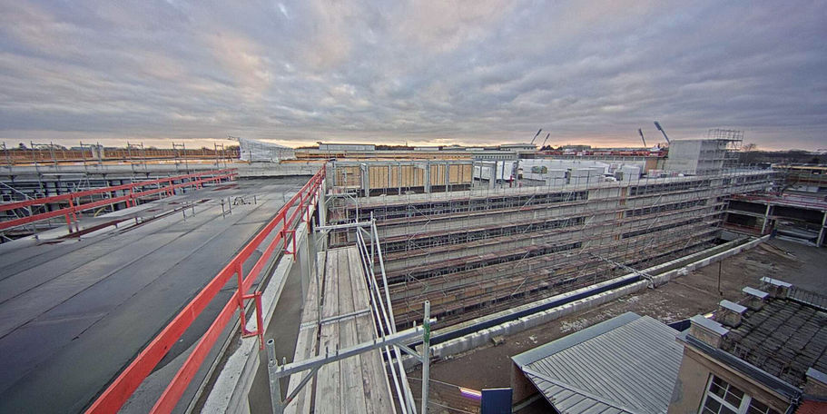 Blick auf den Neubau der Zentralen Medizinischen Funktionen am Abend des 6. März 2018. Im Hintergrund sind die Flutlichtmasten des Ostseestadions zu sehen - davor oben auf dem Rohbau der Hubschrauberlandeplatz. © 2018 Betrieb für Bau und Liegenschaften Mecklenburg-Vorpommern