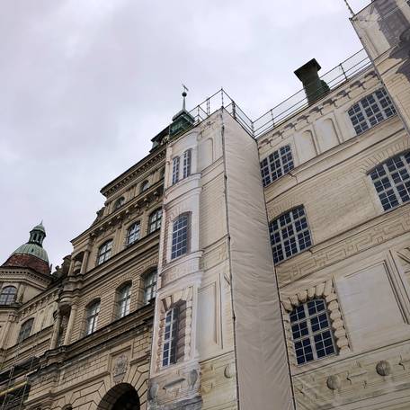 Das eingerüstete Schloss wird während der Bauzeit optisch durch bedruckte Gerüstplanen mit Schlossansichten aufgewertet. © 2021 SBL Schwerin