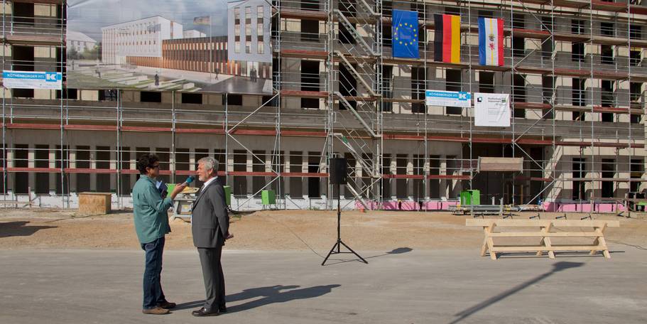 Zwei Männer im Gespräch vor dem eingerüsteten Rohbau des MOC. © 2018 Betrieb für Bau und Liegenschaften Mecklenburg-Vorpommern
