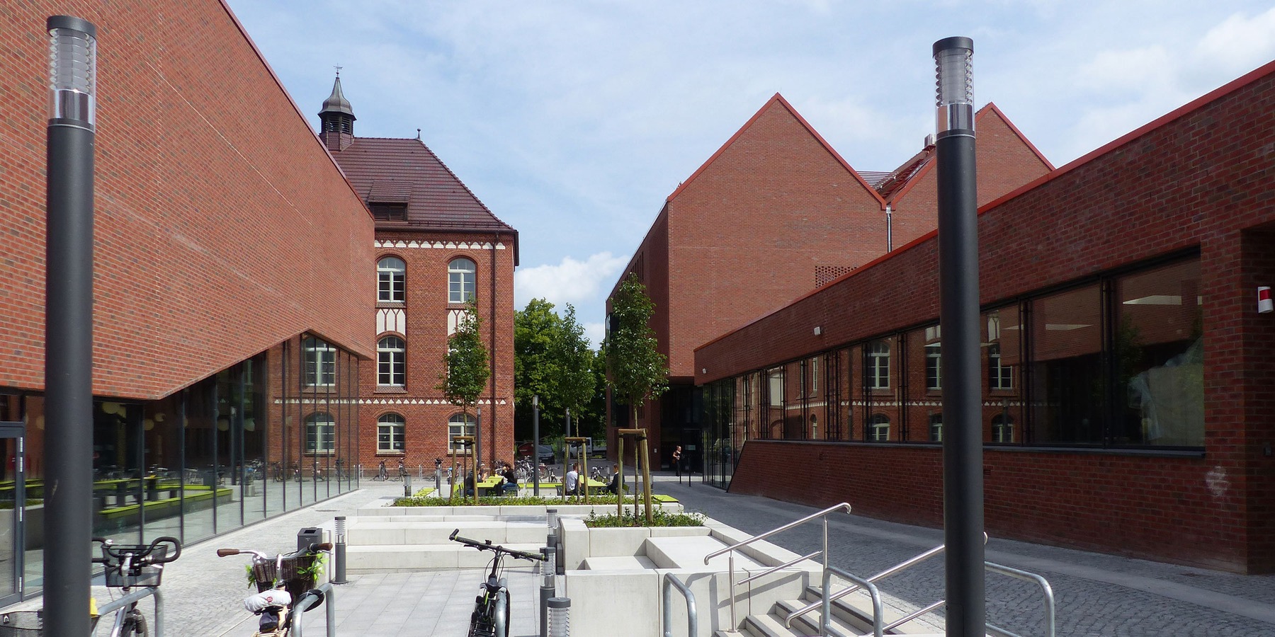 Grüne Bänke als Sitzgelegenheiten zwischen Cafeteria und Hörsaalgebäude bieten  auch im sonnigen Außenbereich eine hohe Aufenthaltsqualität. © 2018 Betrieb für Bau und Liegenschaften Mecklenburg-Vorpommern
