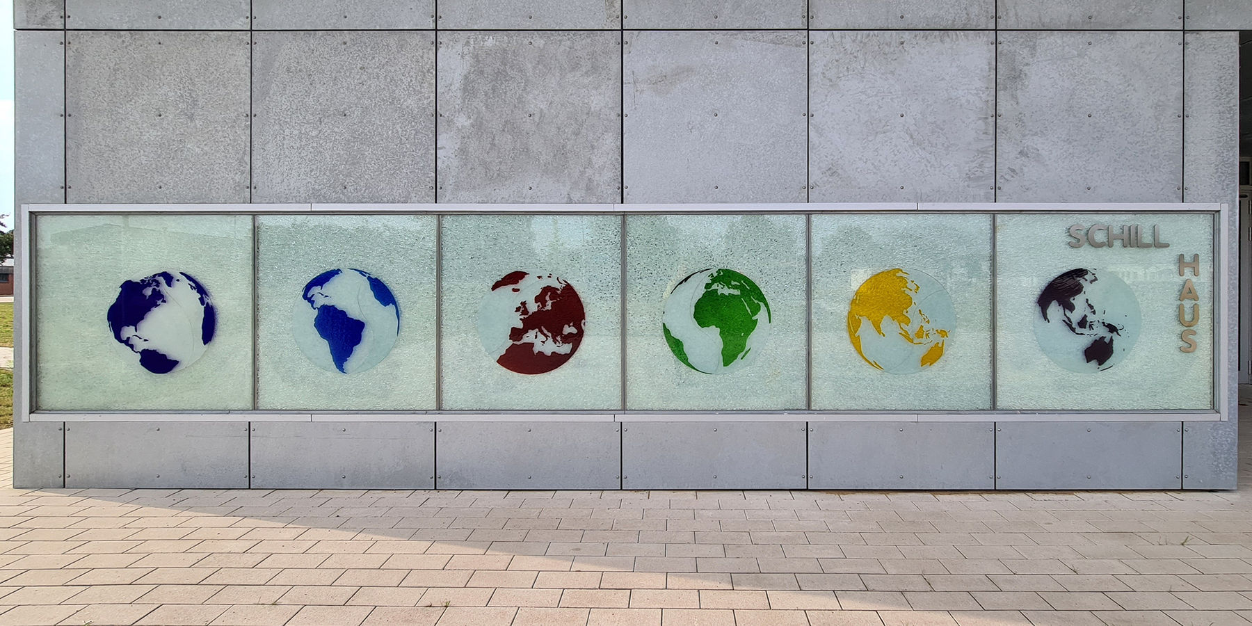 Blick auf das Hausschild mit den sechs Kontinenten – der Künstler Olaf Thaler:  Die sechs globalen Ansichten vermitteln zudem die zentrale  Achse , um die sich die Welt bei aller Vielfalt von Land und Leuten dreht. Das farbige Glas betont die Schönheit, d © 2021 SBL Neubrandenburg