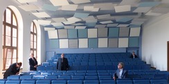Architekt Dipl.-Ing. Ehrenfried Kebe erläutert die Grundidee bei seiner Gestaltung des historischen Hörsaales: mit der Farbe Blau und den scheinbar  wie willkürlich / zufällig  angeordneten Akustik-Pendeln und Absorber-Elementen im Wand- und Deckenbereich © 2022 SBL Greifswald