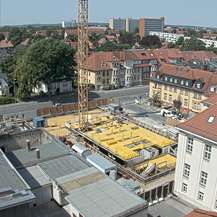 Blick auf eine Baustelle. Ein Kran steht in der Bildmitte. Im Hintergrund sind Häuser und der Horizont zu sehen. © 2022 SBL Schwerin