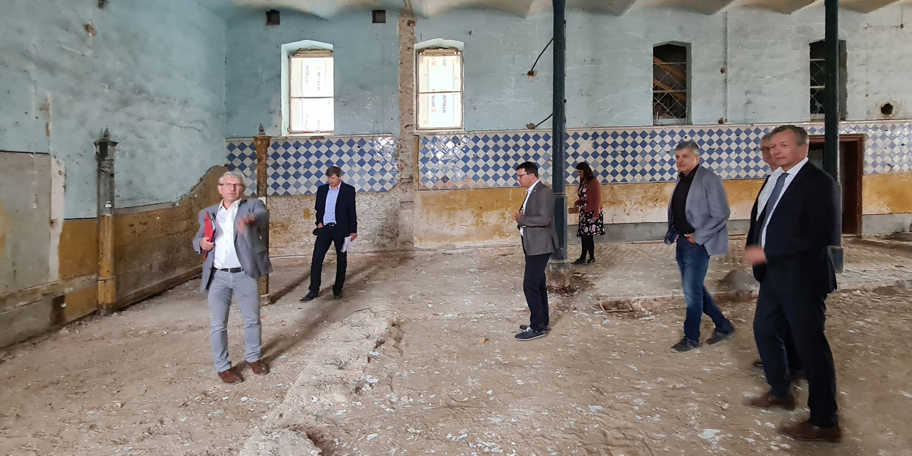 Herr Tasler (l) erläutert die geplanten Bauarbeiten in der ehemaligen Stallung des Südflügels – links im Hintergrund ist noch eine historische Pferdebox erhalten. © 2022 SBL Neubrandenburg