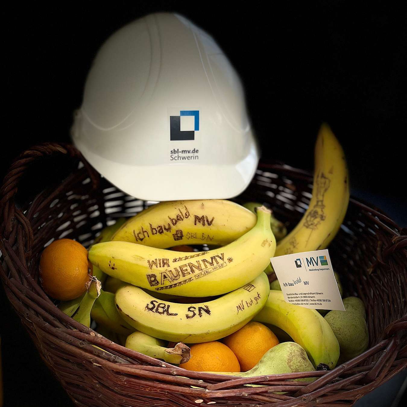 Schutzhelm mit Bildmarke der Staatlichen Bau- und Liegenschaftsverwaltung Mecklenburg-Vorpommern auf einem Korb mit Bananen und Orangen. © 2022 Janine Chlebek (Finanzministerium MV / SBL-MV)