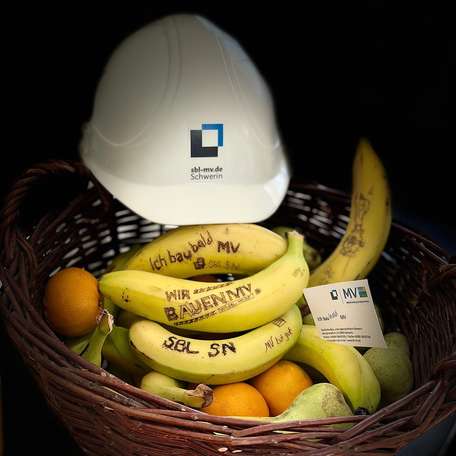 Schutzhelm mit Bildmarke der Staatlichen Bau- und Liegenschaftsverwaltung Mecklenburg-Vorpommern auf einem Korb mit Bananen und Orangen. © 2022 Janine Chlebek (Finanzministerium MV / SBL-MV)