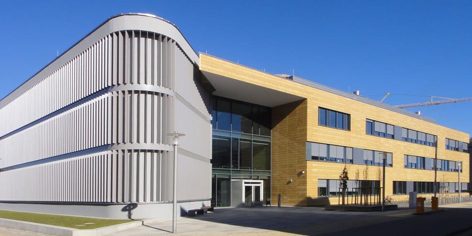 Blick von Südwesten auf den Neubau C_DAT - Das markante, abgerundete südwestliche Bauteil mit vertikaler Aluminiumlamellen-Verkleidung betont den angrenzenden Haupteingangsbereich © 2015 Christian Hoffman, FM M-V