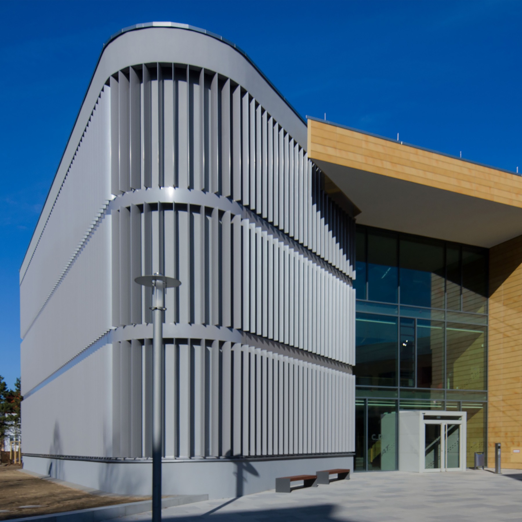 Blick von Südwesten auf den Neubau C_DAT - Das markante, abgerundete südwestliche Bauteil mit vertikaler Aluminiumlamellen-Verkleidung betont den angrenzenden Haupteingangsbereich © 2015 Christian Hoffman, FM M-V