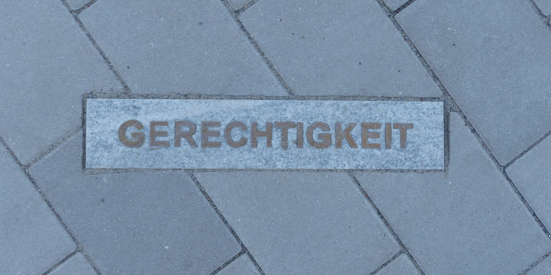 20 eingelassene Granitsteine, davon 12 helle mit positiven Begriffen aus der Polizeiarbeit (z.B. AUFKLÄRUNG, HILFE, GERECHTIGKEIT …) in der Pflaster- bzw. Rasenfläche vor dem Eingang sind Bestandteil der 4-teiligen Kunst am Bau-Installation © 2023 SBL Greifswald