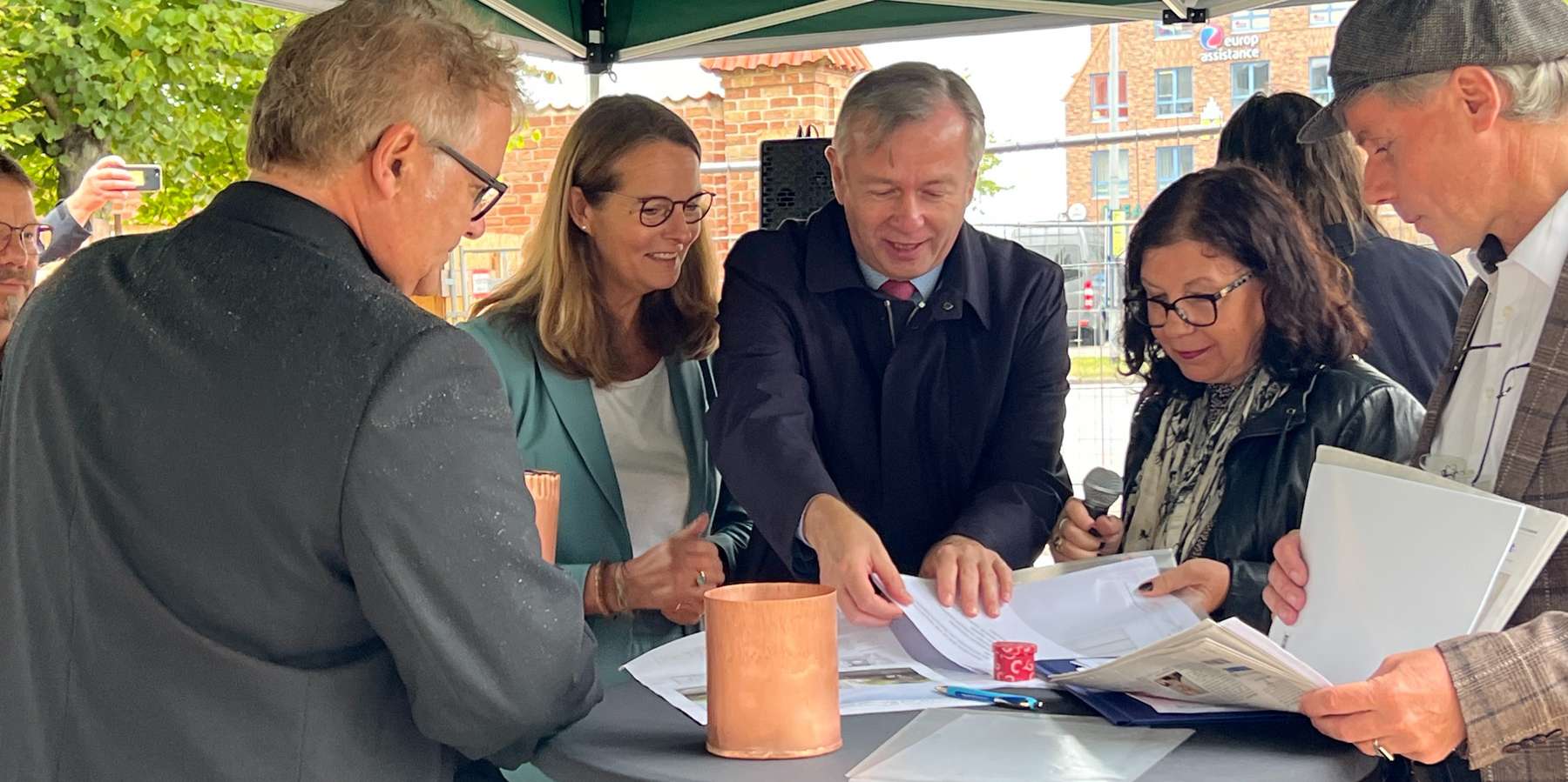 Die Kartusche wird nach traditionellem Brauch mit tagaktuellen Utensilien - Urkunde, Bauplänen, Baubeschreibung, Ostseezeitung und Münzen bestückt. © 2023 Christian Hoffmann (Finanzministerium M-V / sbl-mv)