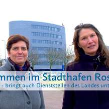 Carmen-Alina Botezatu (re.) leitet das SBL Rostock und ist mit Sandra Auris (li.), Sachbearbeiterin Liegenschaftsmanagement im SBL Rostock, für die Unterbringung der aDiLaS verantwortlich. Im Hintergrund: Gebäude am Stadthafen in Rostock – dort ist u. a. © 2024 Christian Hoffmann (sbl-mv / Finanzministerium MV)