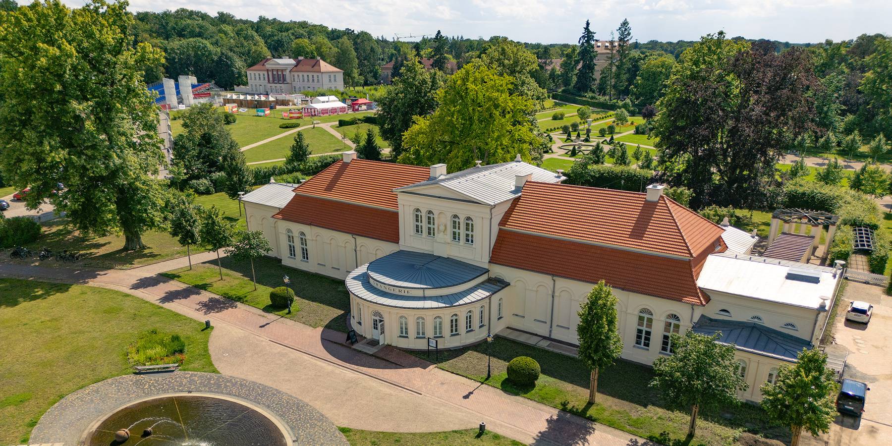 Blick auf den Vorplatz, die östliche Fassade und das Dach der Orangerie im Vordergrund sowie den Schlossgarten und das Kavalierhaus im Hintergrund. © 2024 Christian Hoffmann (sbl-mv / Finanzministerium MV)