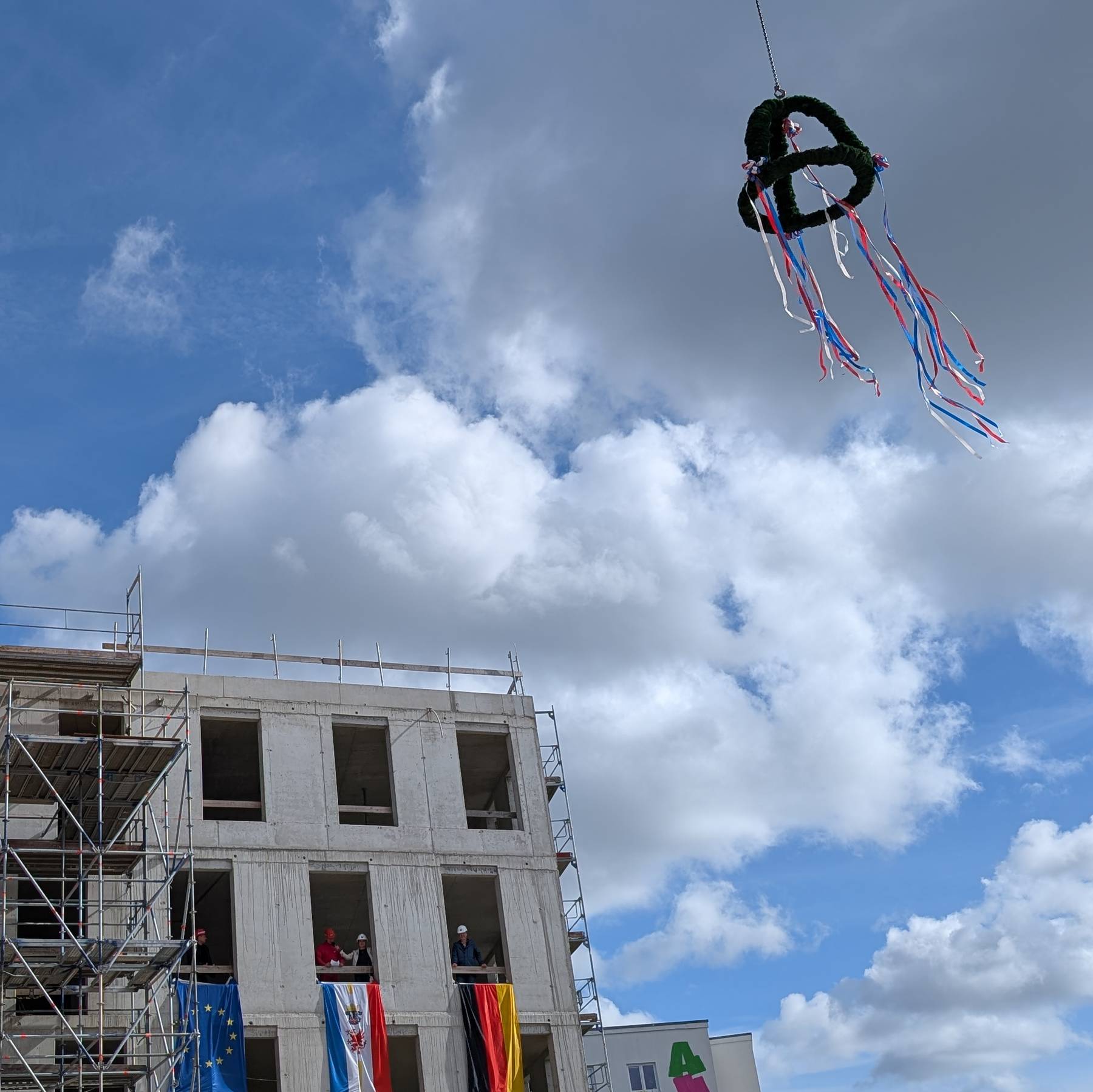 Die Richtkrone schwebt über dem Verwaltungsgebäude während der Polier Herr Siegmund den Richtspruch verliest. © 2025 SBL Rostock