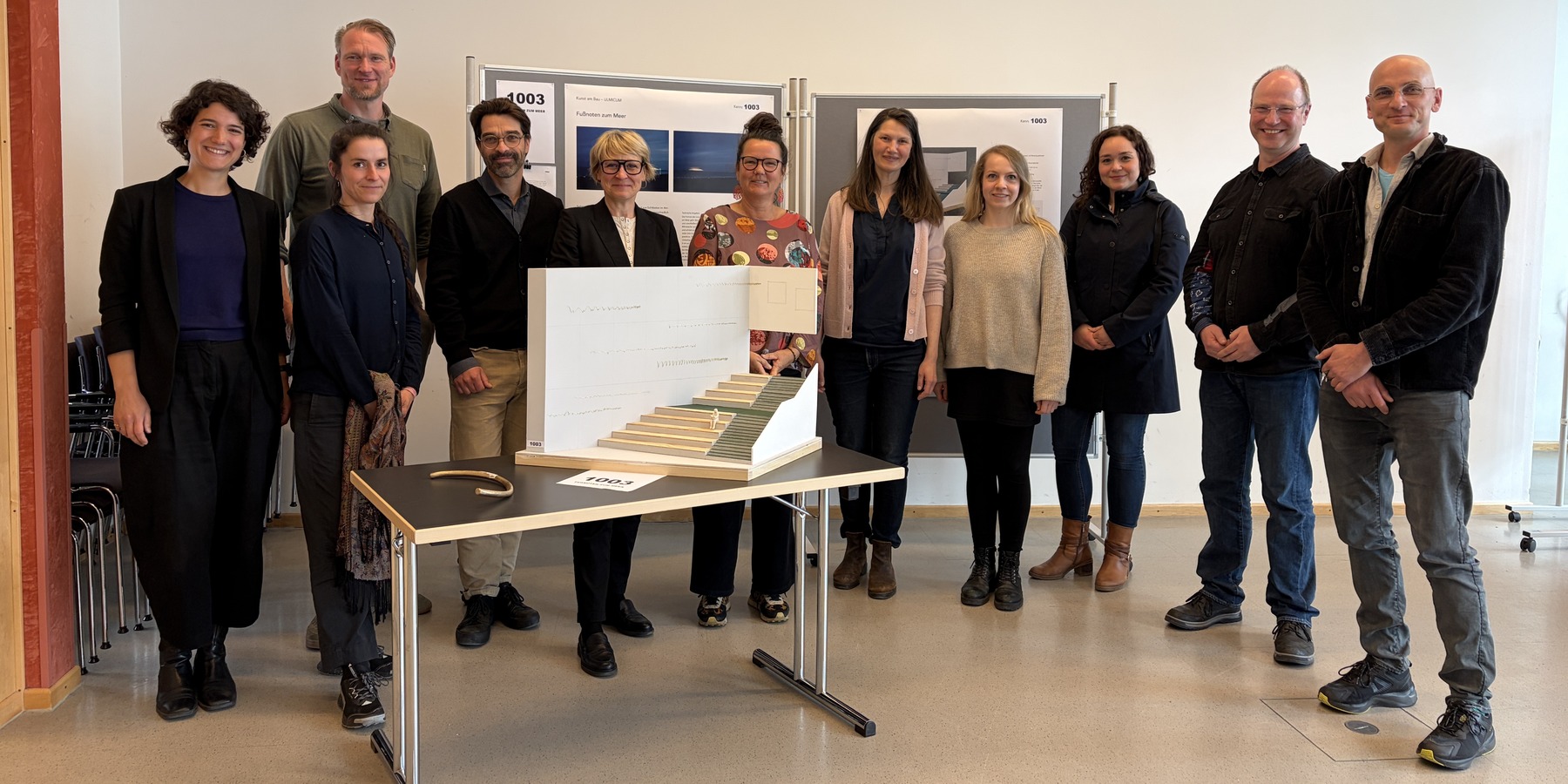 Das Preisgericht vor dem Siegerentwurf (von links: Ilana Zorbas, Marike Schreiber, Tino Bittner, Bernd Jaeger, Synke Schmolinski, Takwe Kaenders, Carmen-Alina Botezatu, Catleen Hofbauer, Lisa Krebes, Andreas Boye und Mathias Goldberg). © 2026 SBL Rostock