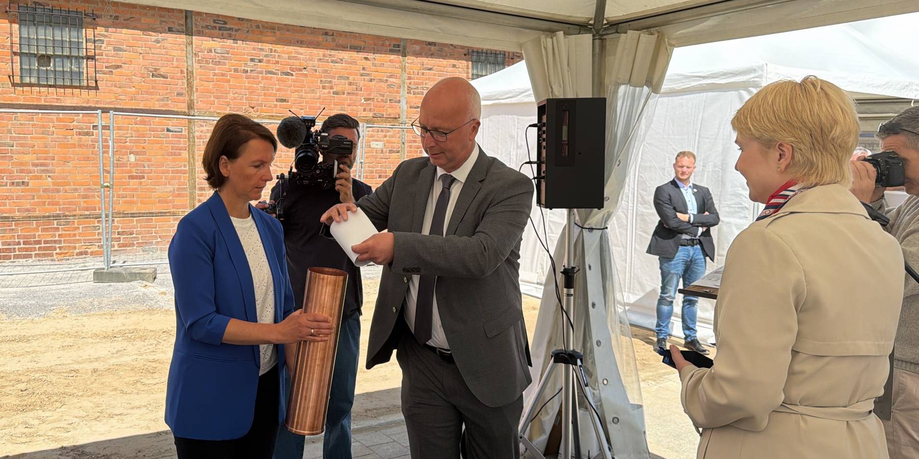 Die Kartusche wird gefüllt: Projektleiterin Anja Niemann vom SBL Schwerin und Leiter Dr. Andreas Werner füllen die Kartusche. Ministerpräsidentin Manuela Schwesig (rechts im Bild) legte eine Münze des Landes MV in die Kartusche. © 2026 Christian Hoffmann (SBL-MV / Ministerium für Finanzen und Digitalisierung MV)