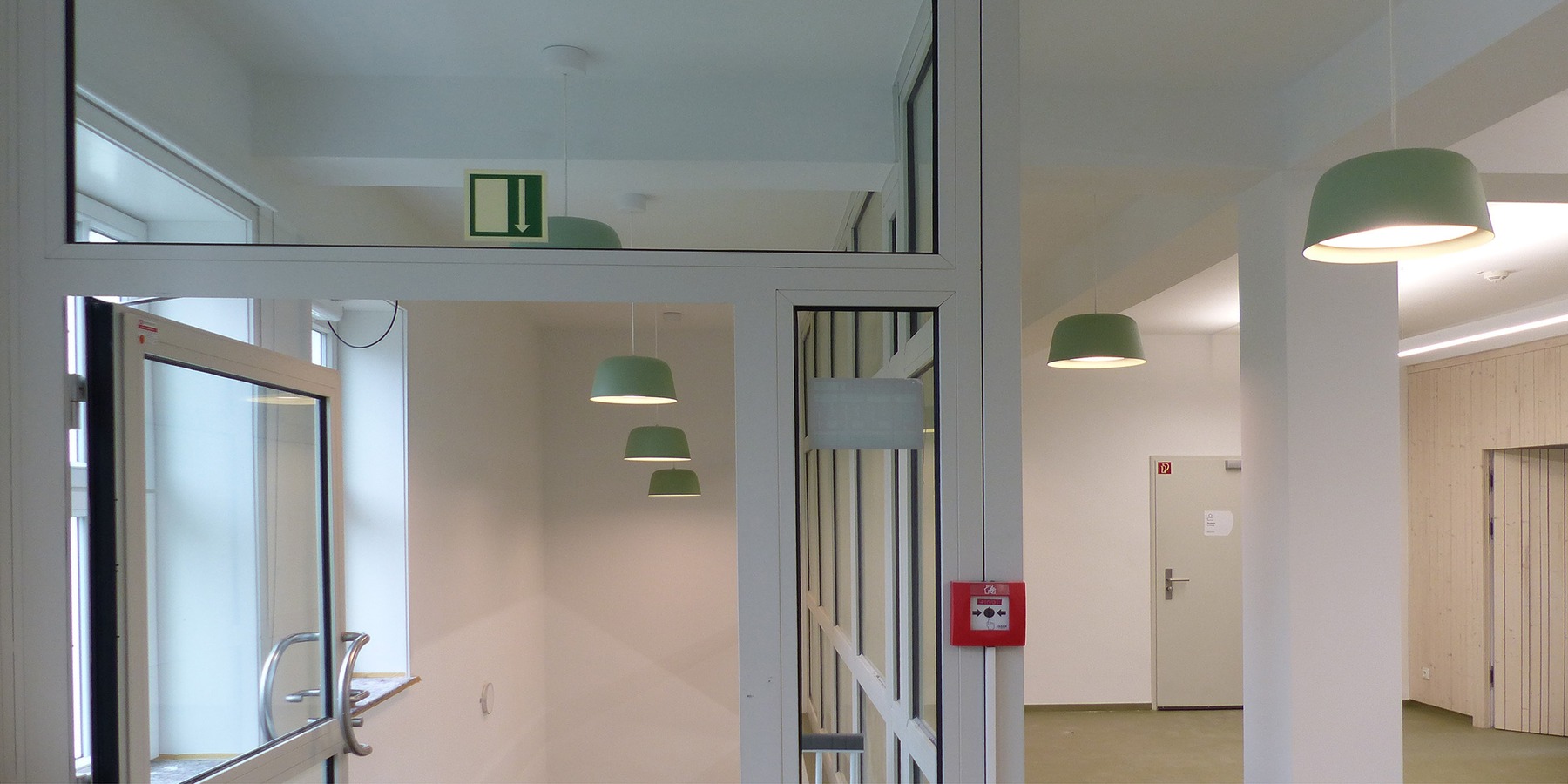 Helle und freundliche Flure mit modernem Lichtkonzept, hellen Holzverkleidungen und grünem Lineoleum prägen die Bibliothek im Bestand und im Neubau © 2026 SBL Greifswald