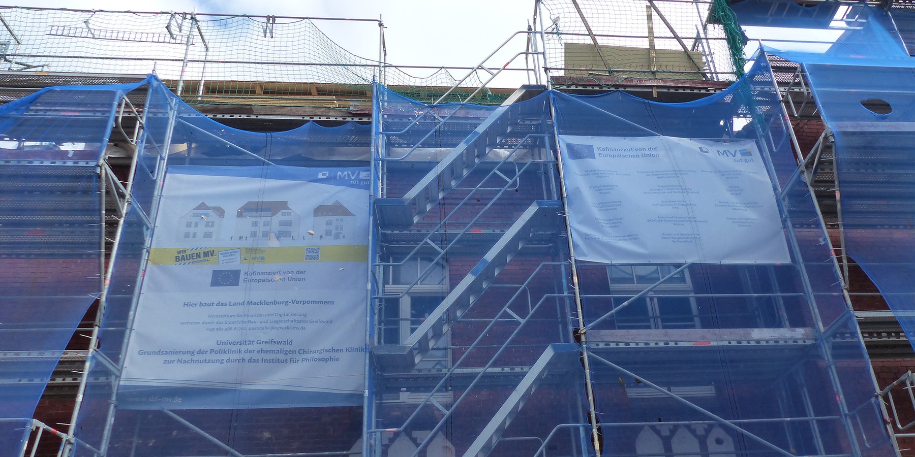 Bautenstand Juli 2026: Eingerüstete Südfassade mit Bauschildern © 2026 SBL Greifswald