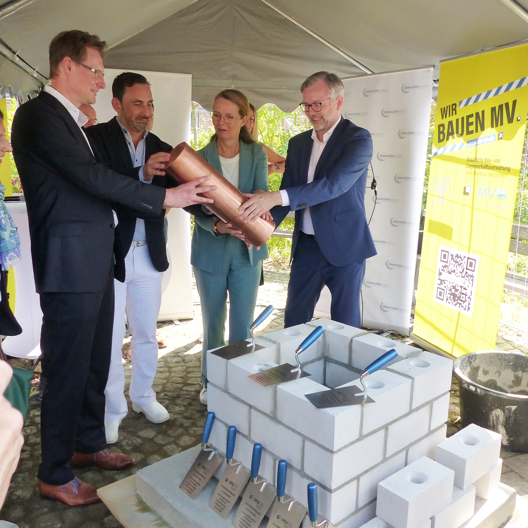 Gemeinsam wird die verschlossene Kartusche in den vorbereiteten Grundstein gesetzt, v.l.n.r.: Prof. Dr. Dr. Adrian Schwarzer, Prof. Dr. med. Stephan Kersting, Bettina Martin und Dr. Heiko Geue © 2026 SBL Greifswald