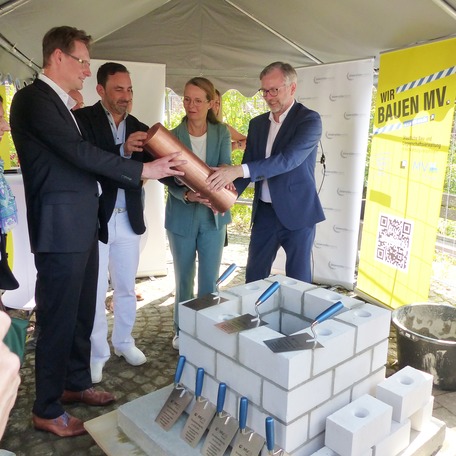 Gemeinsam wird die verschlossene Kartusche in den vorbereiteten Grundstein gesetzt, v.l.n.r.: Prof. Dr. Dr. Adrian Schwarzer, Prof. Dr. med. Stephan Kersting, Bettina Martin und Dr. Heiko Geue © 2026 SBL Greifswald